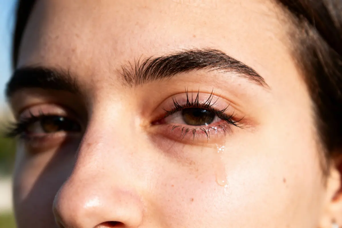 Gros plan d'un œil humain pleurant, sourcils foncés et peau claire, en lumière naturelle.