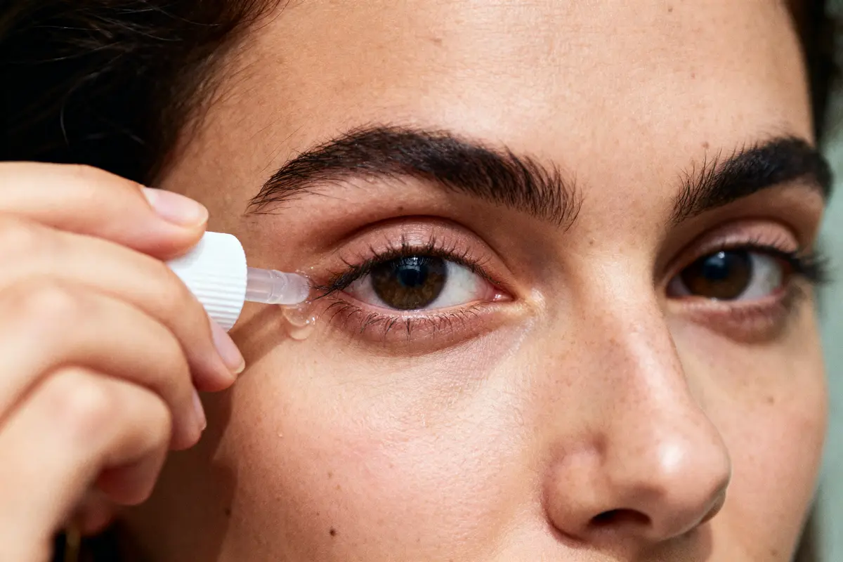 Gros plan d'une personne appliquant une goutte pour les yeux à l'aide d'un flacon compte-gouttes.